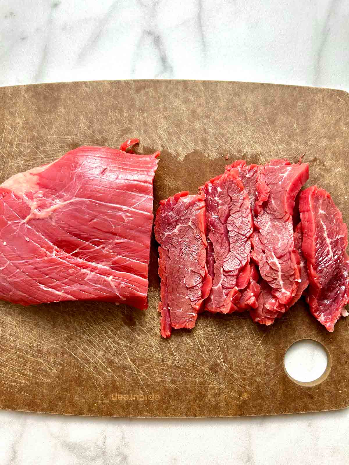 flank steak being cut across the grain into ¼ inch slices.