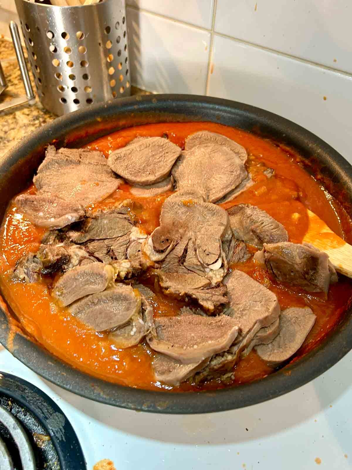 slices of braised beef tongue on top of tomato sauce in pan.