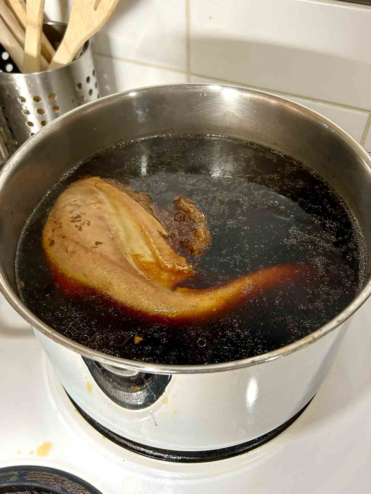 beef tongue being braised in pot of dark liquid.