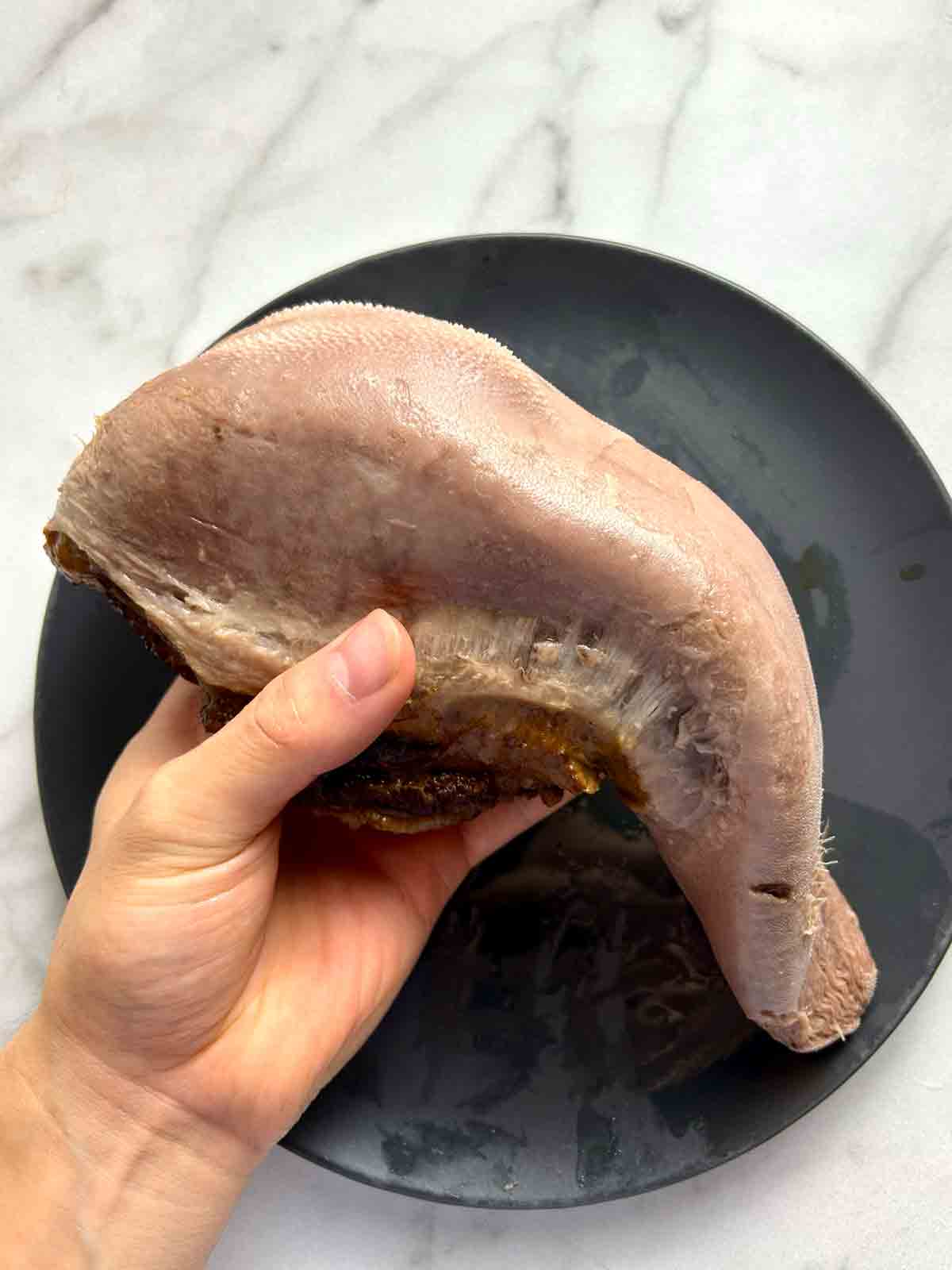 hand holding beef tongue with skin peeled off.