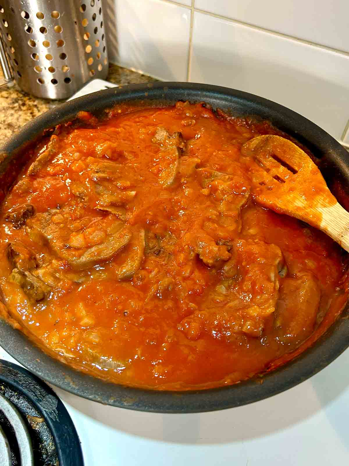 beef tongue slices being mixed into tomato sauce in pan.