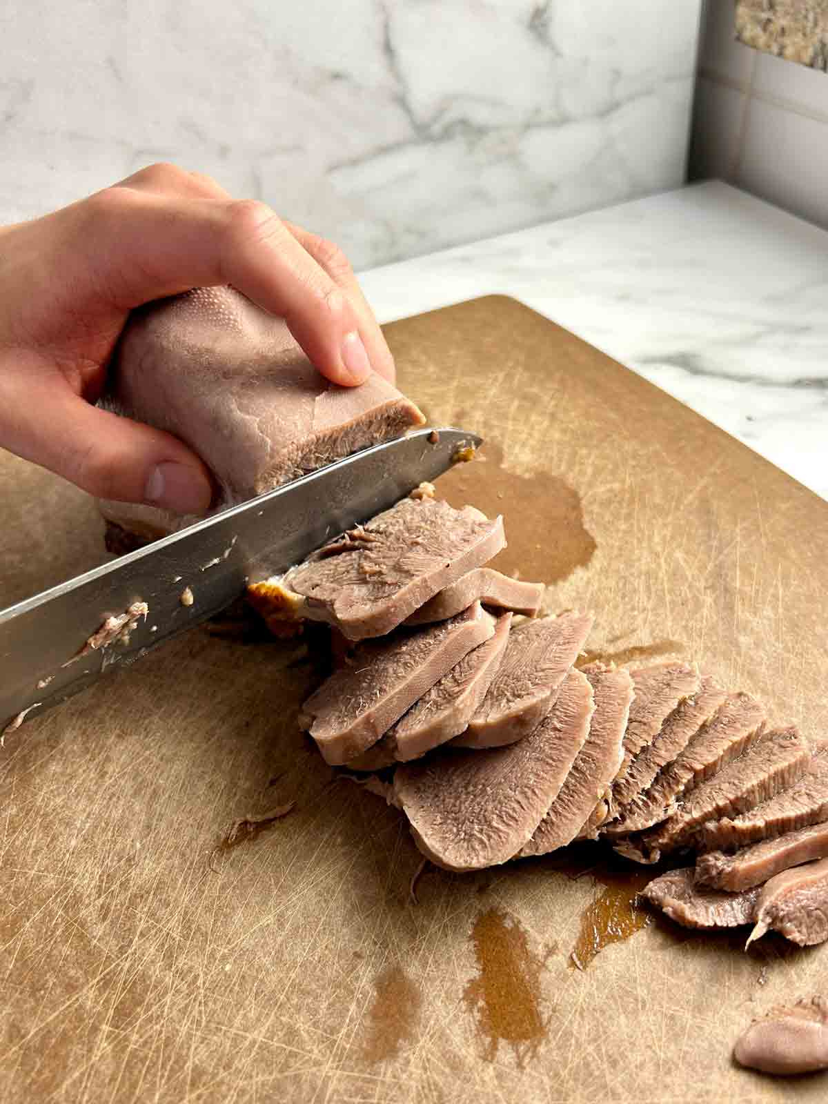 beef tongue being sliced crosswise on cutting board.