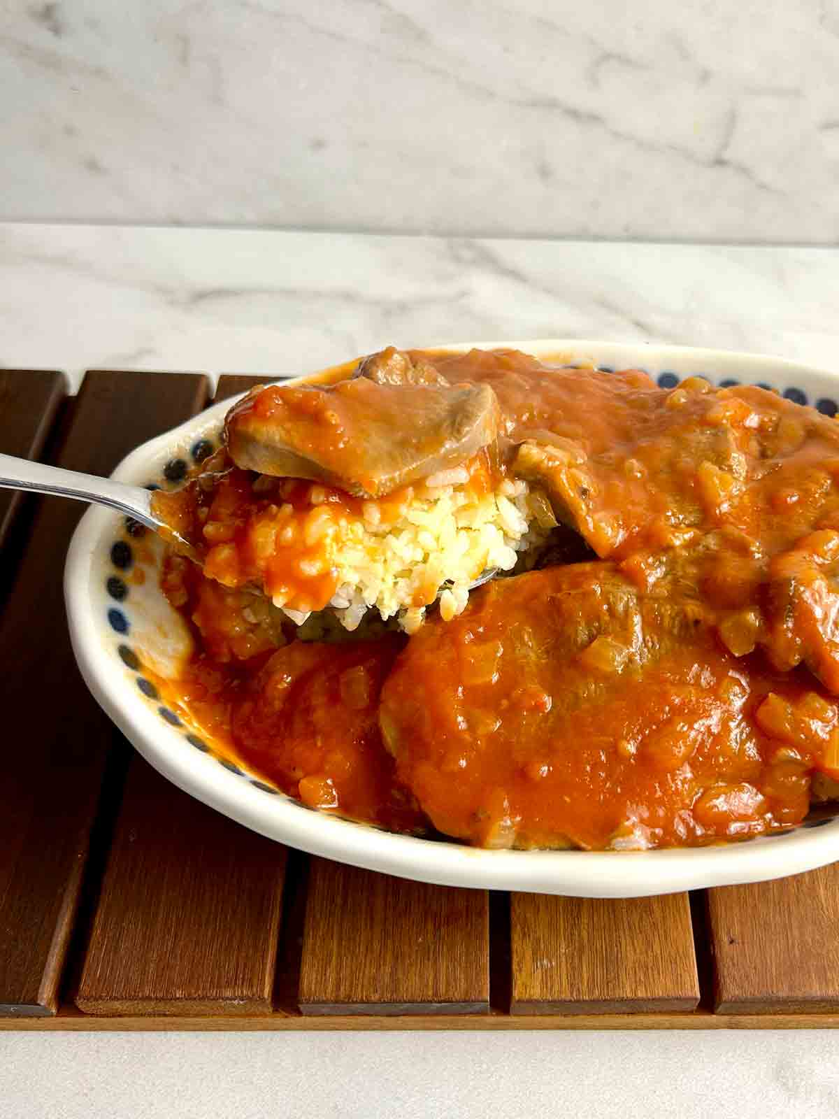 spoon lifting slice of beef tongue with rice and tomato sauce underneath it.