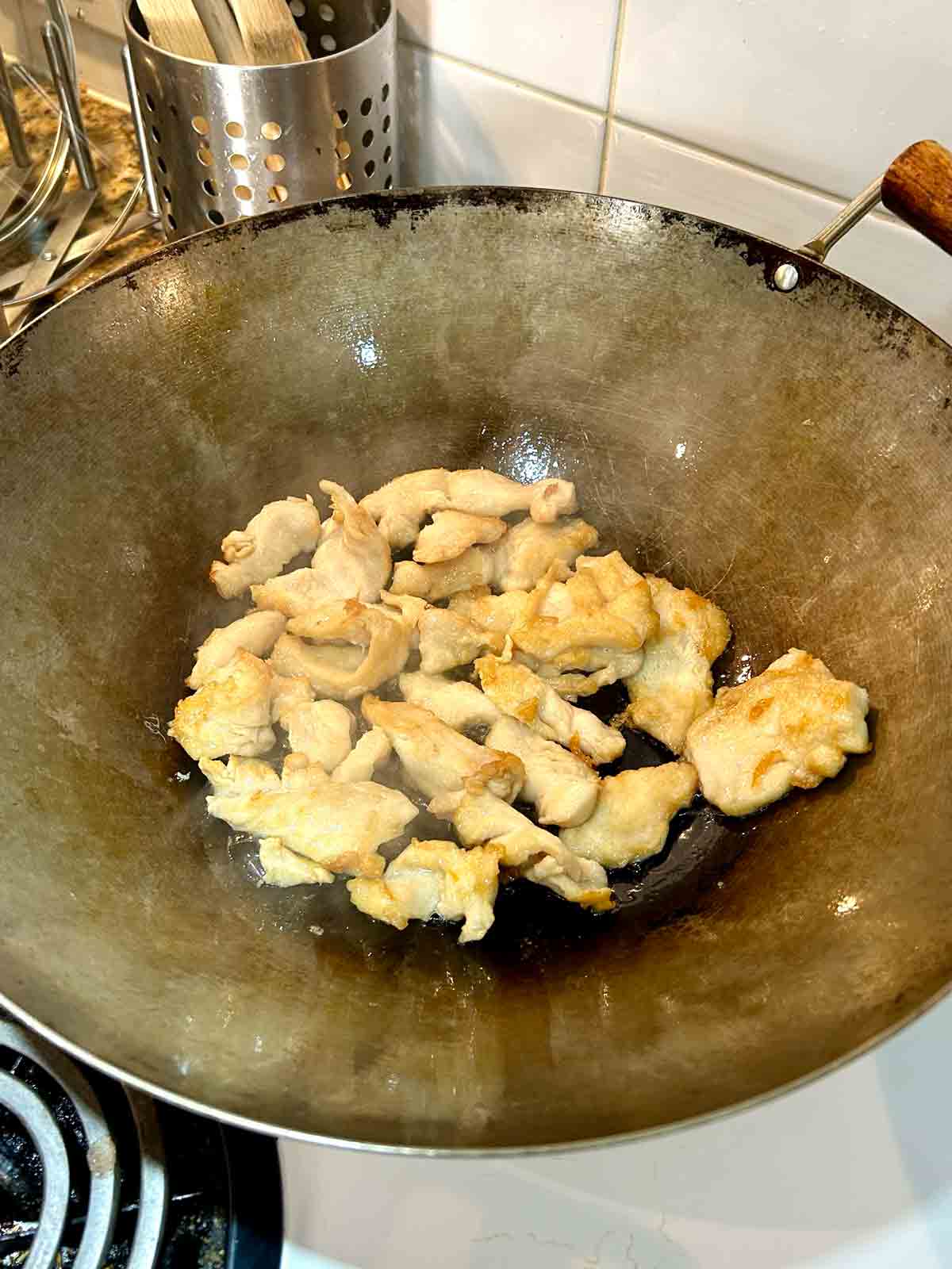 second side of chicken being seared in wok.