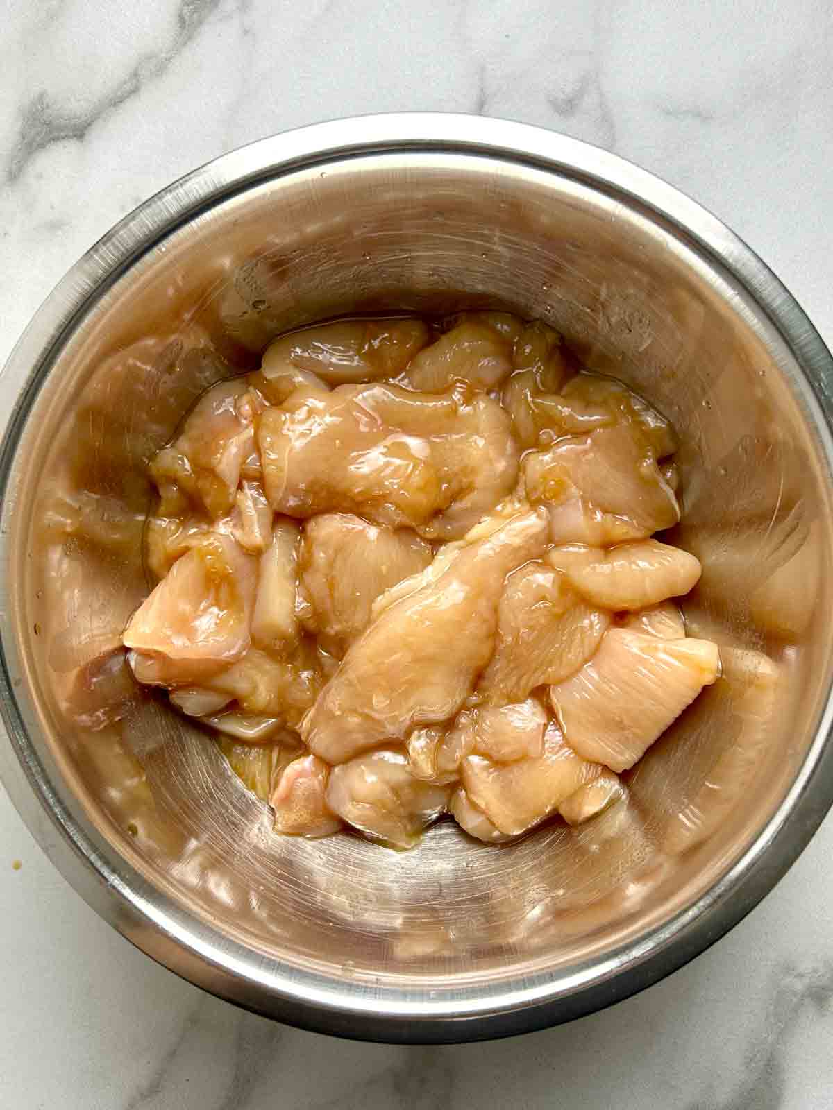 chicken slices being marinated in bowl.