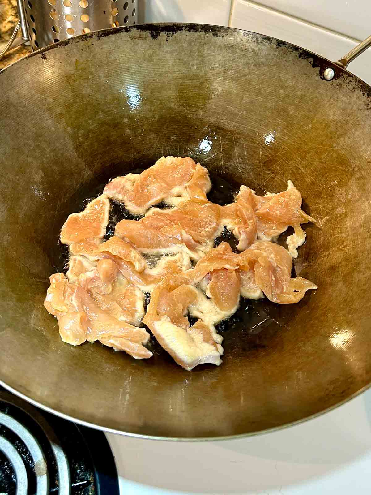 first side of chicken being seared in wok.