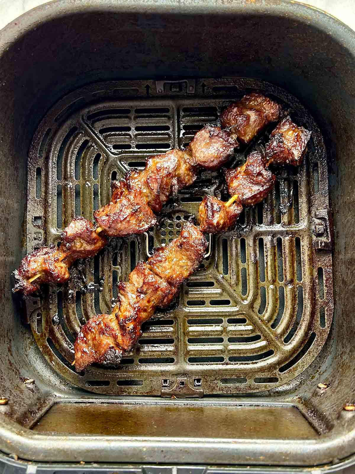 charred beef skewers in air fryer basket.