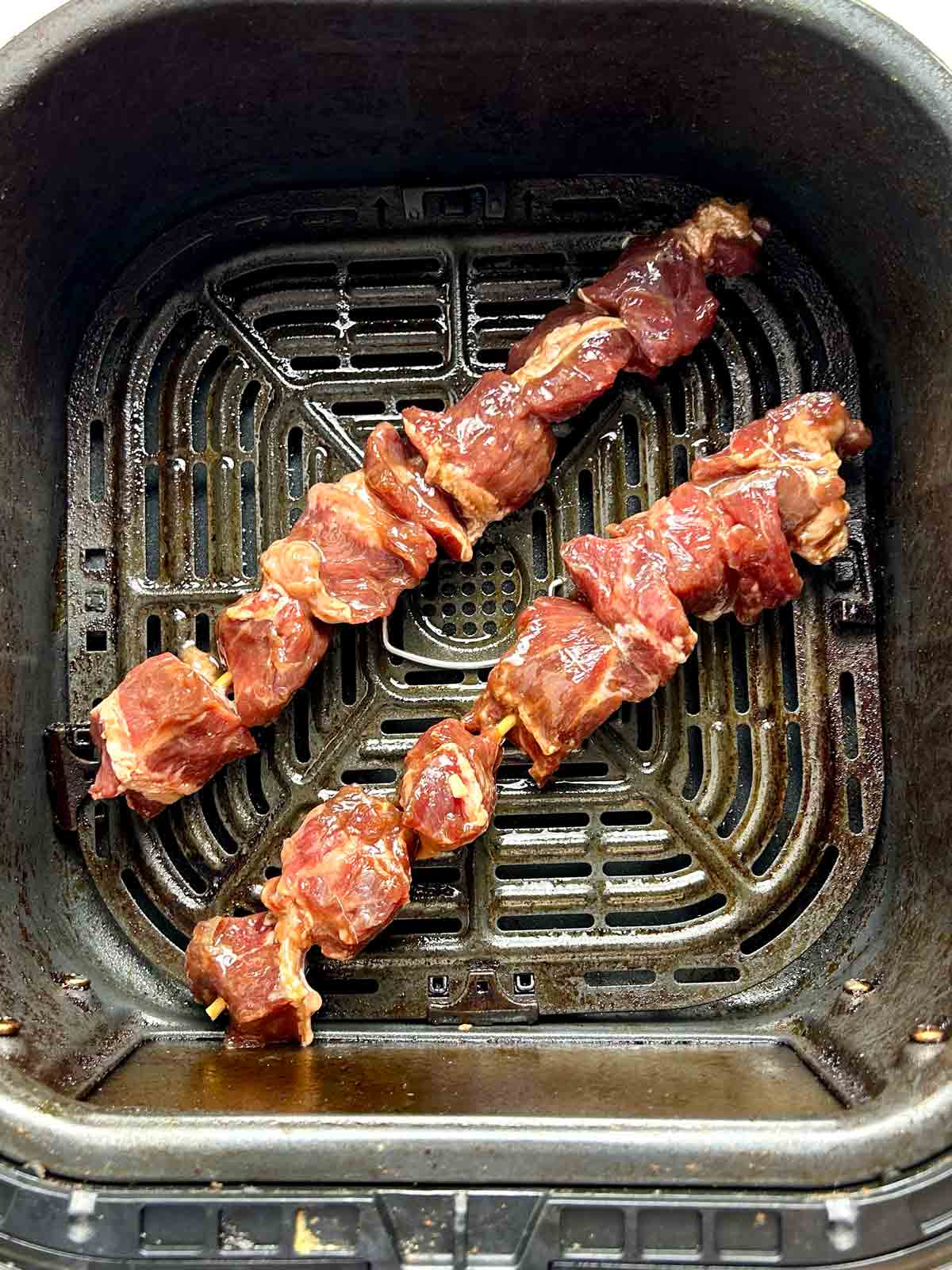 uncooked beef skewers in air fryer basket.