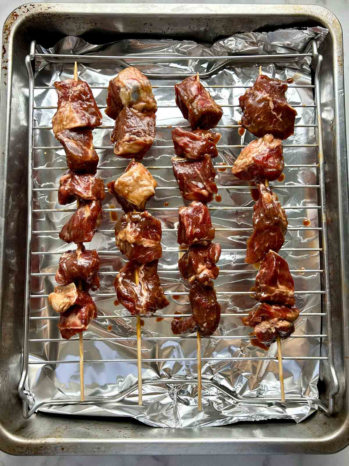 uncooked beef skewers on roasting rack.