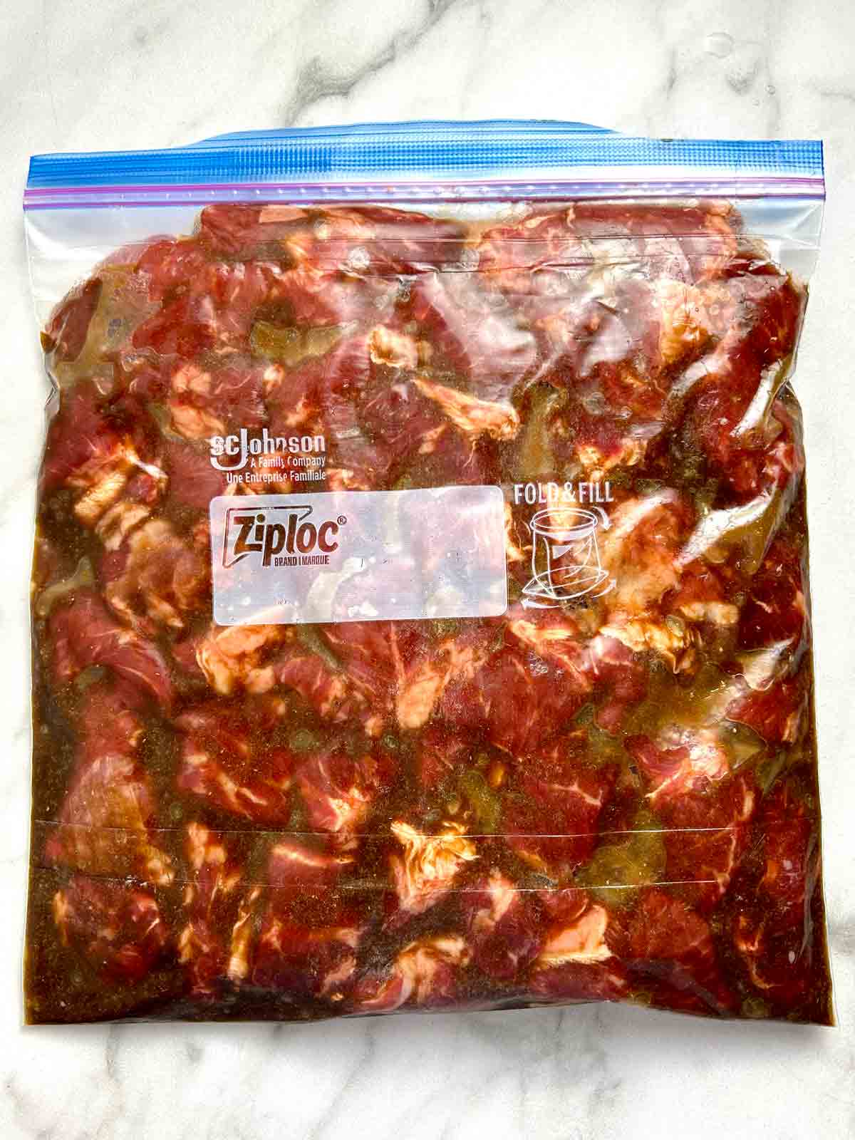 beef cubes being marinated in plastic bag.