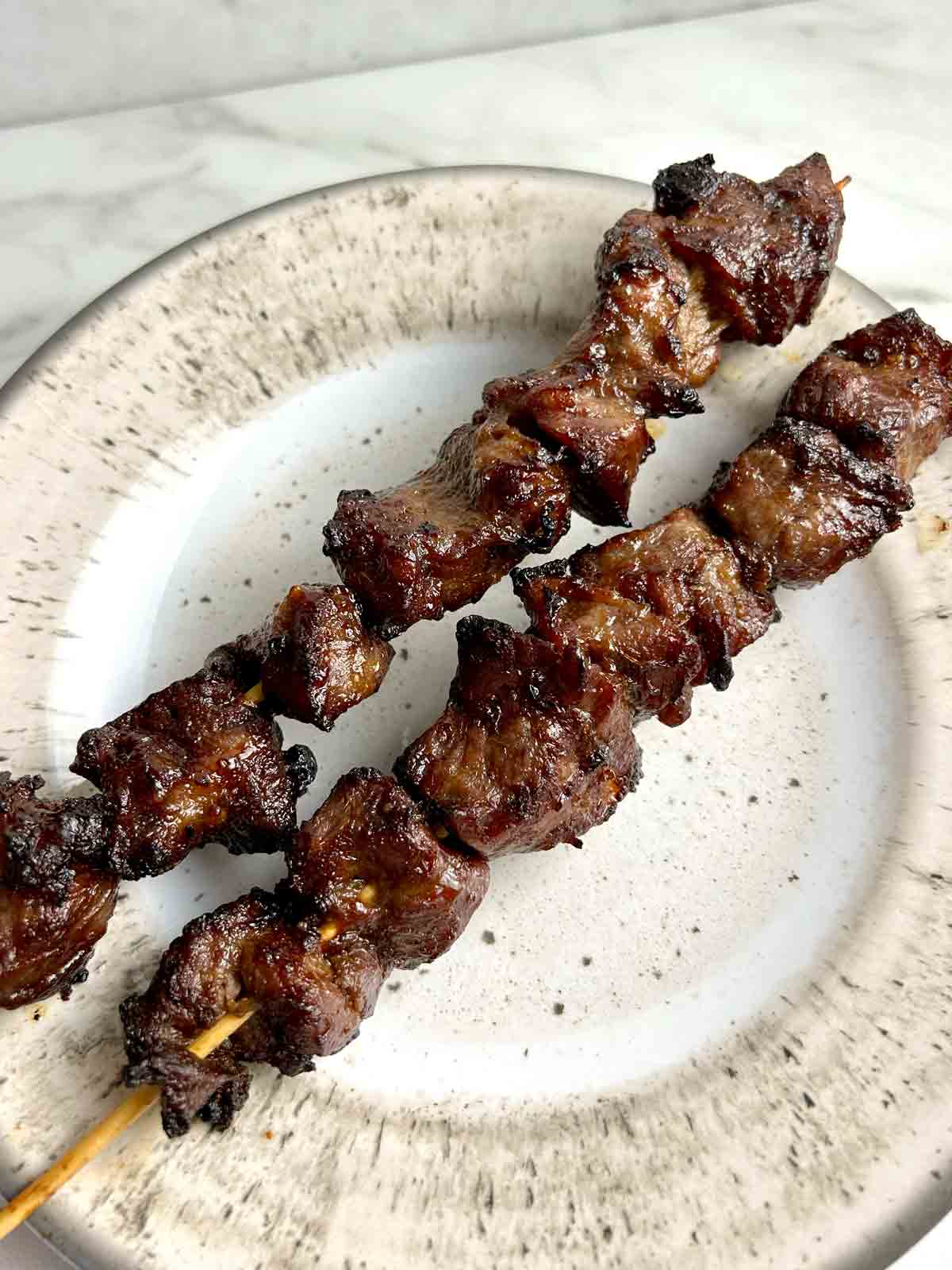 two skewers of beef on a plate.