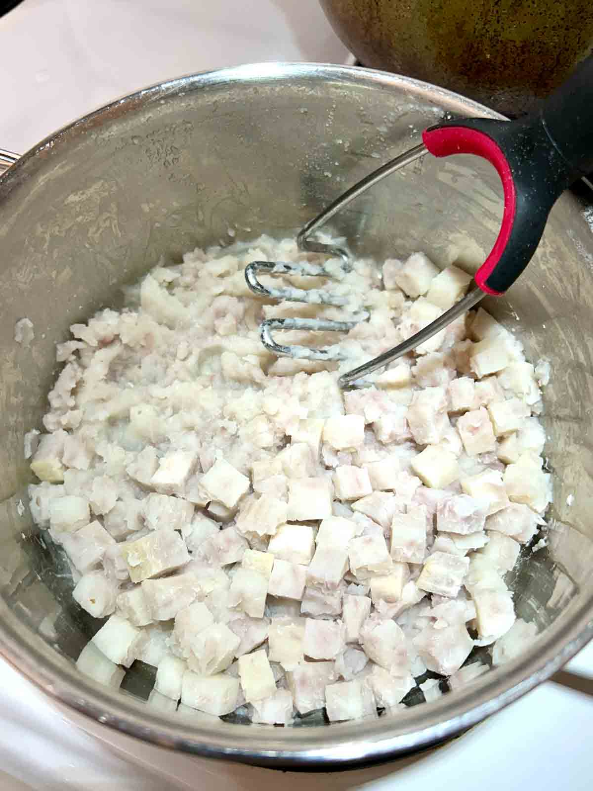 ⅓ of taro being mashed with potato masher.