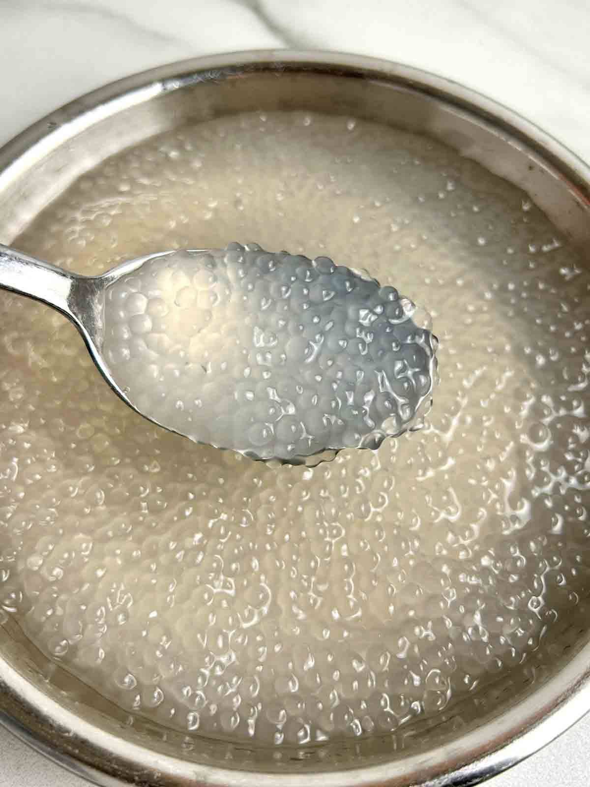 spoon scooping cooked tapioca from bowl of water.