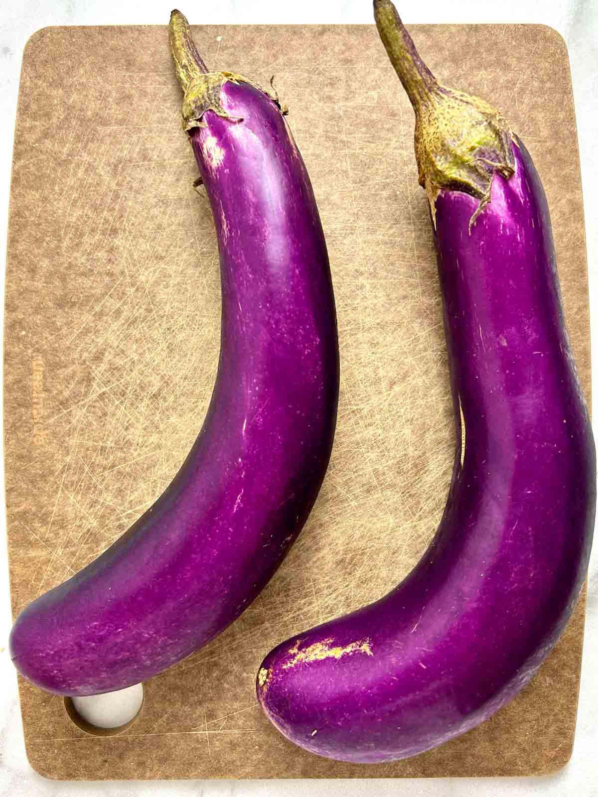 two Chinese eggplants on cutting board.