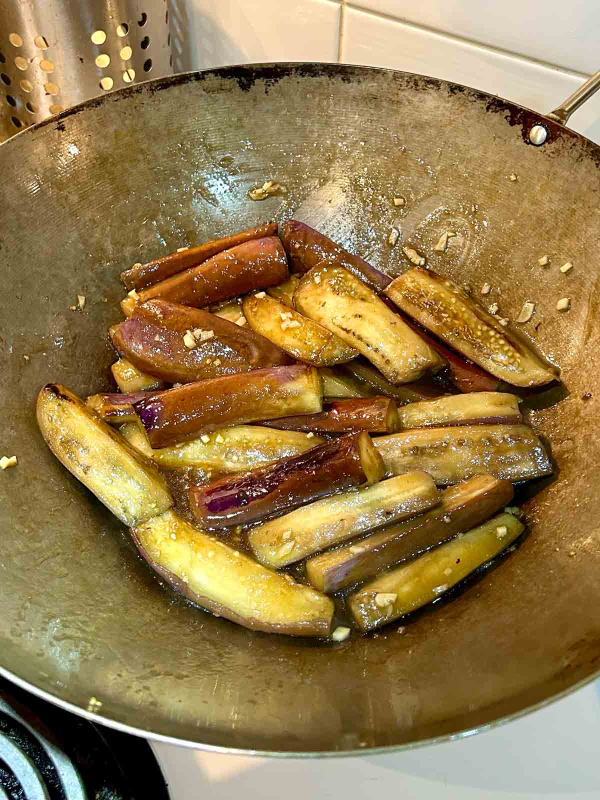 eggplant being tossed with sauce in wok.