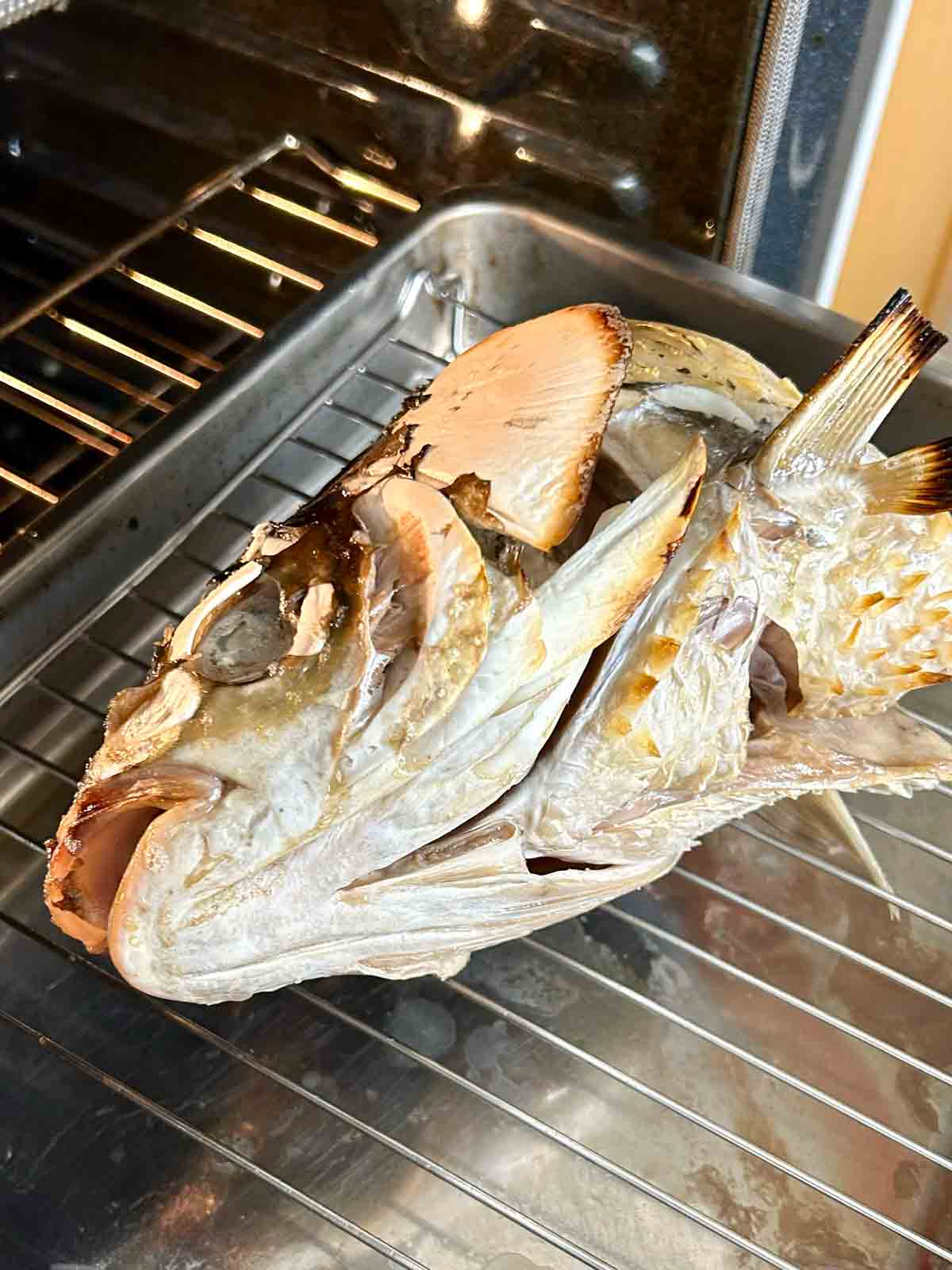 roasted fish head with charred edges on roasting rack.