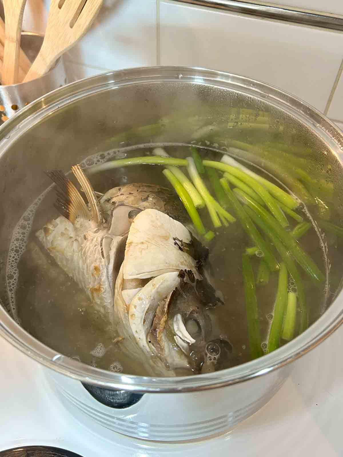 roasted fish head with other soup ingredients in large pot.