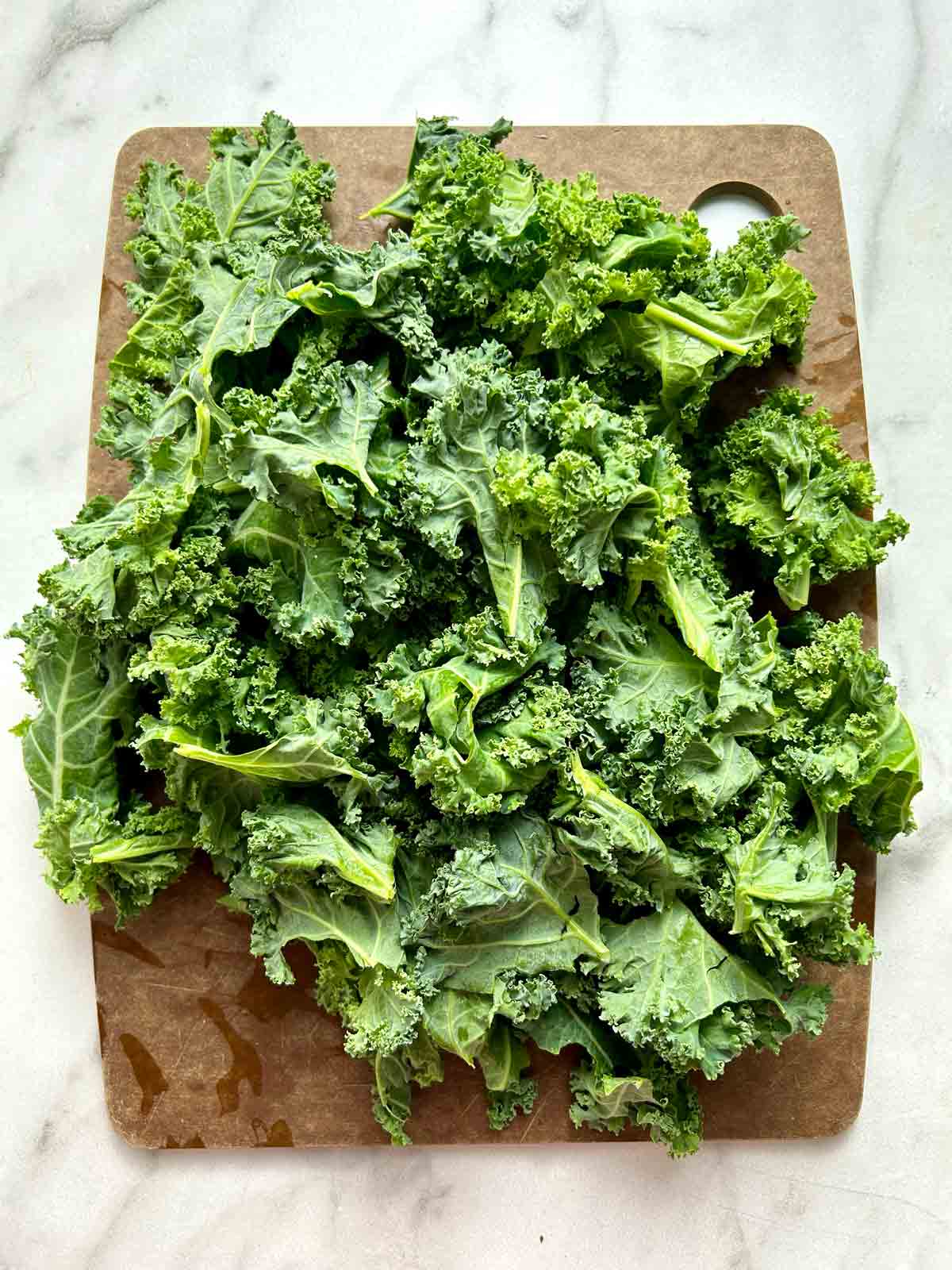 kale leaves torn into bite-sized pieces on cutting board.