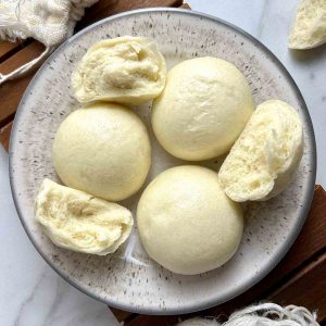 mantou on a plate; some are torn in half to show the fluffy interior.