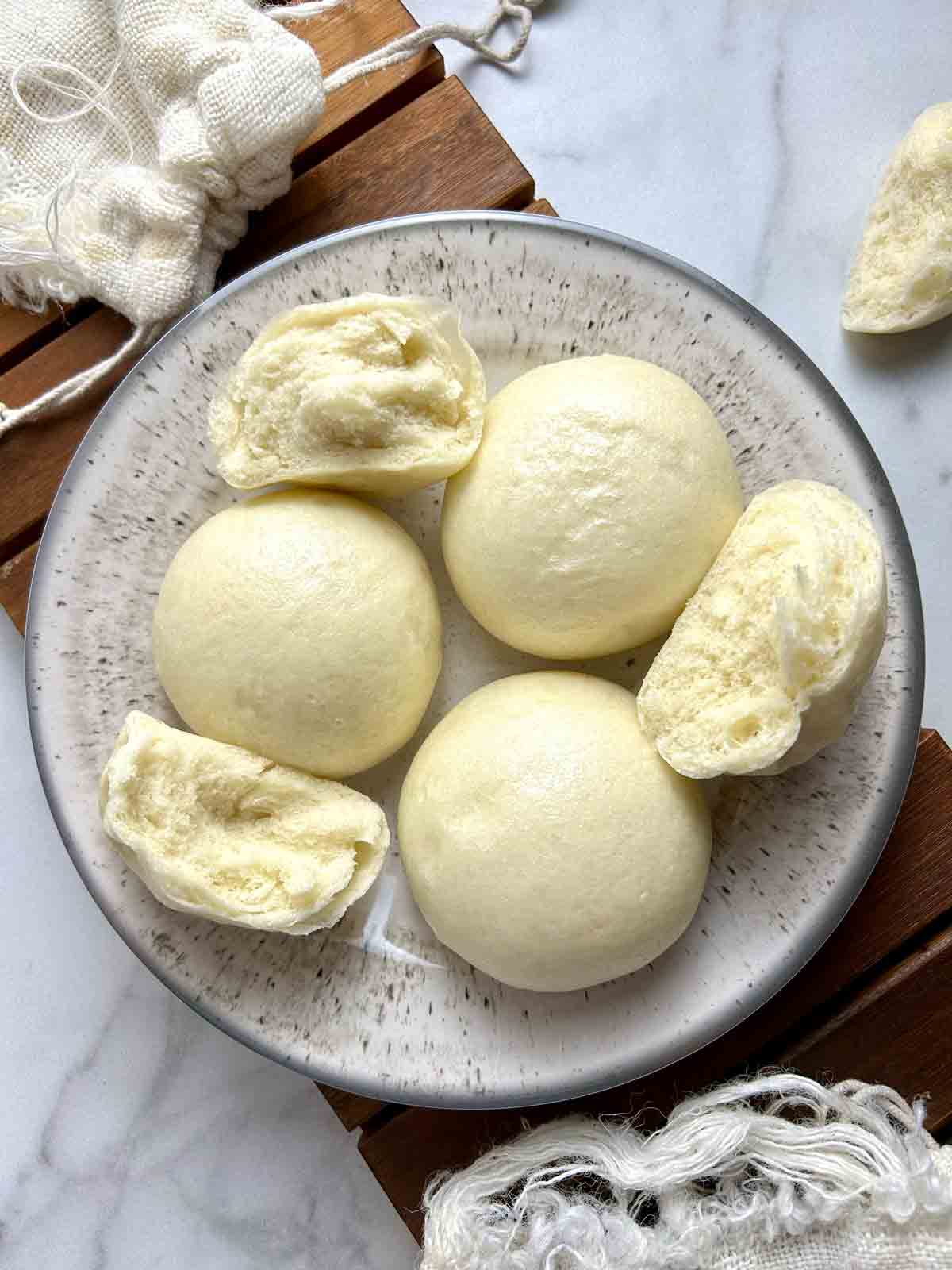 mantou on a plate; some are torn in half to show the fluffy interior.