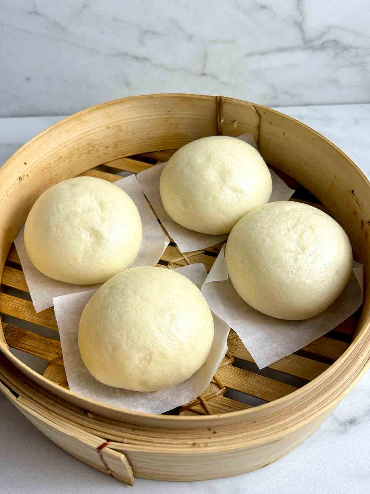 four steamed mantou in bamboo steamer tray.