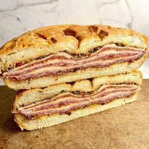 two halves of a muffuletta sandwich sitting on top of each other.