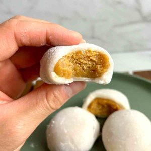 A hand holding a partially eaten piece of peanut butter mochi.