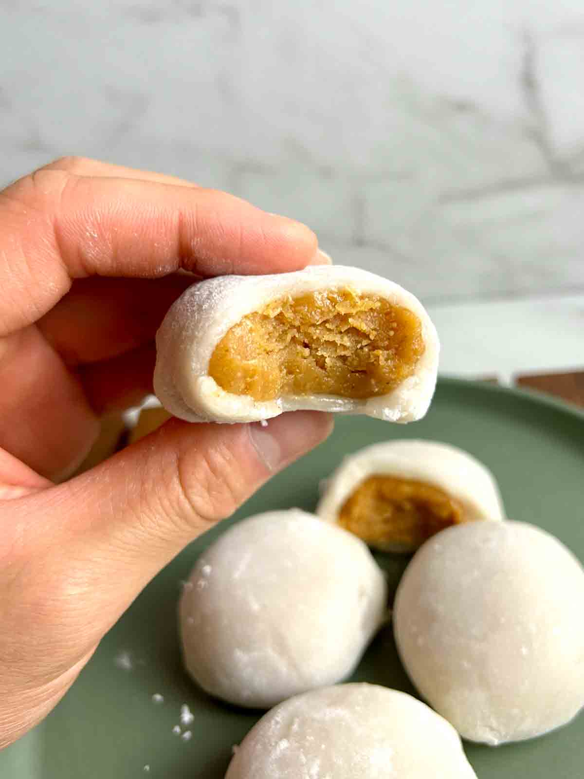 A hand holding a partially eaten piece of peanut butter mochi.