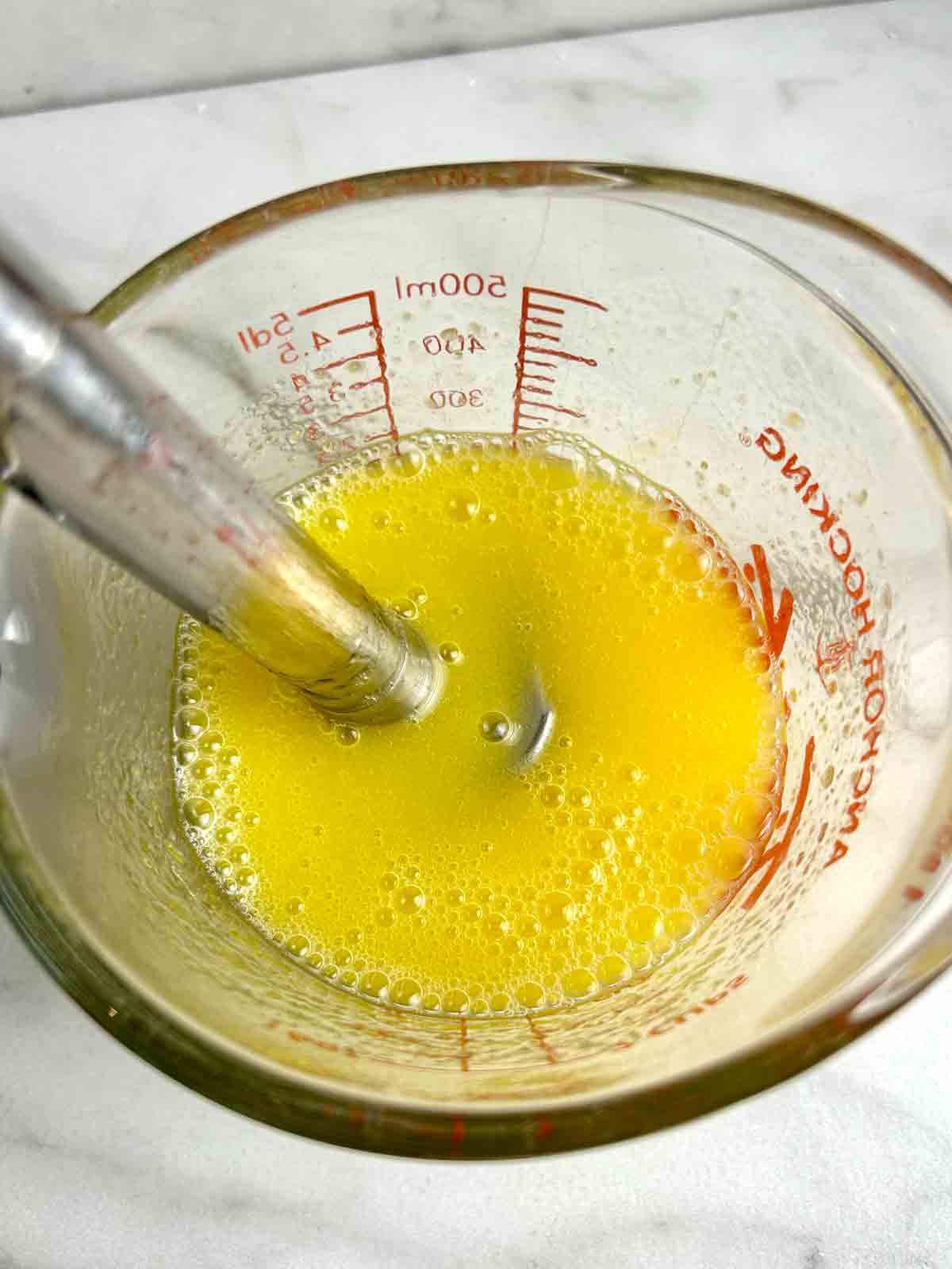 mango juice being blended with sodium alginate in measuring cup.