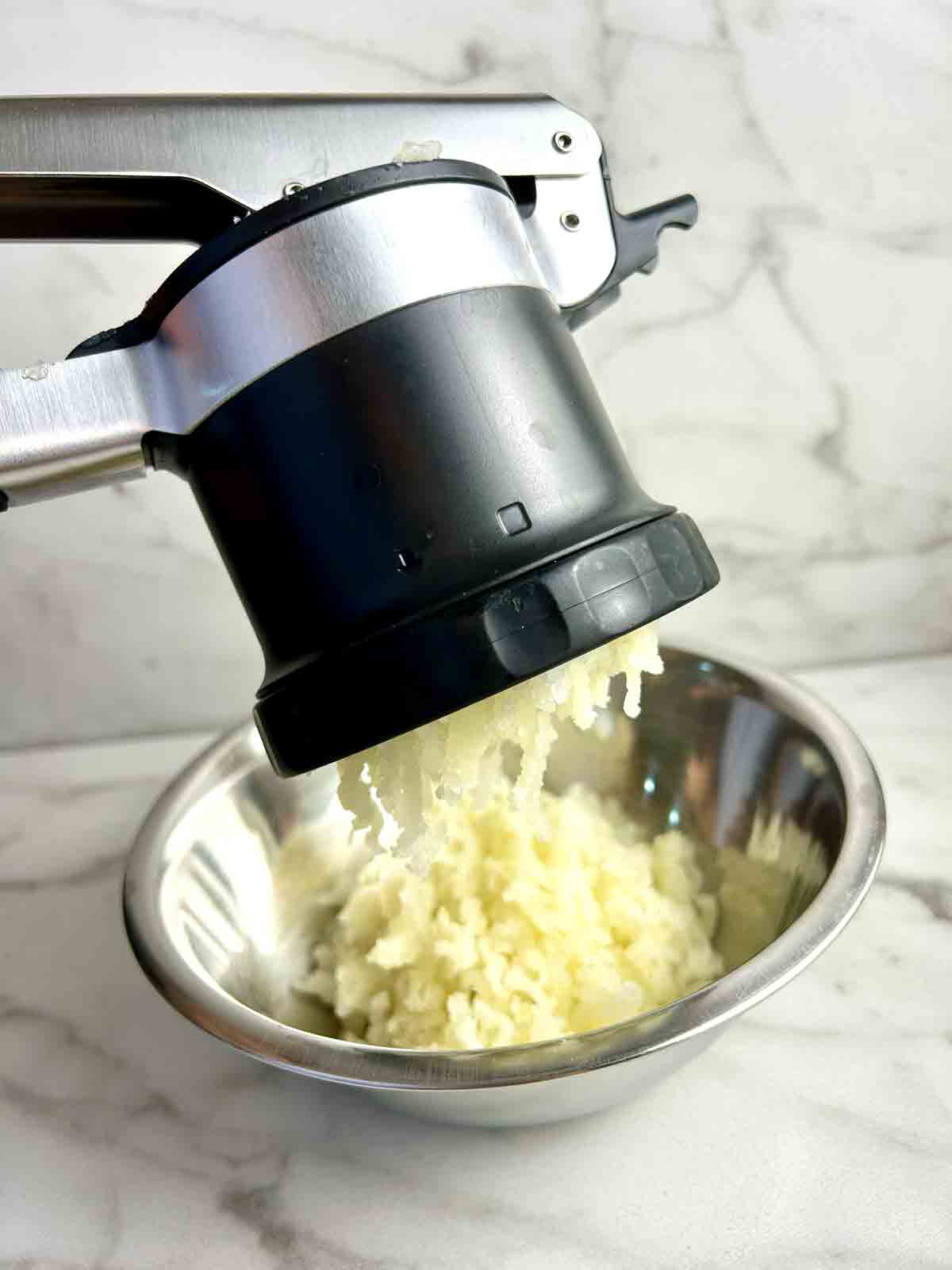 potatoes going through potato ricer.