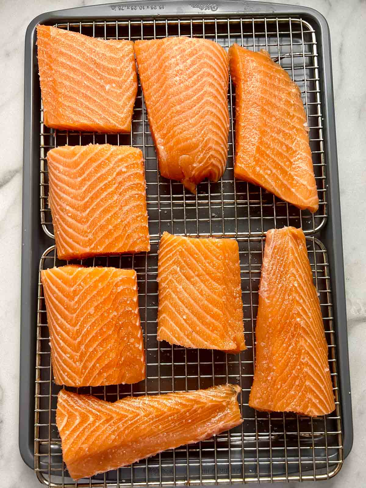 salmon portions being cured in salt and sugar on wire rack.