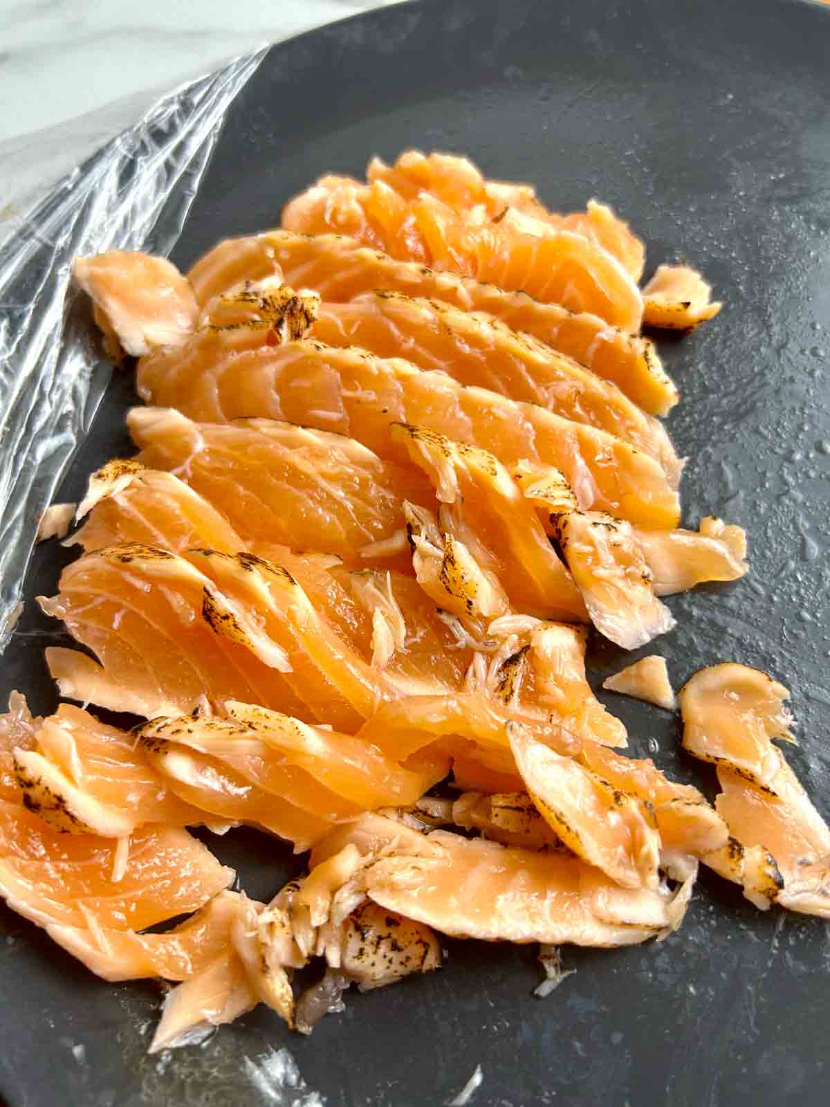 messy slices of salmon tataki with many uneven and broken pieces.