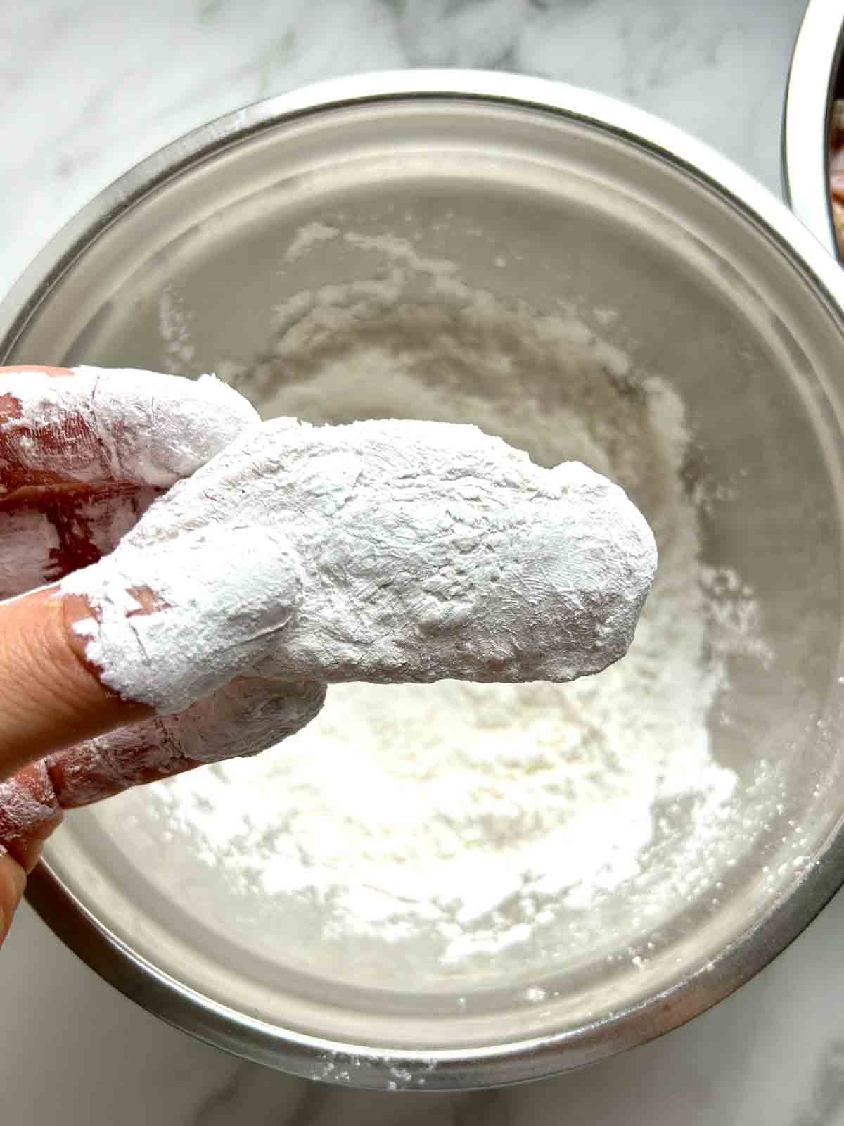 chicken wing being coated in starches.