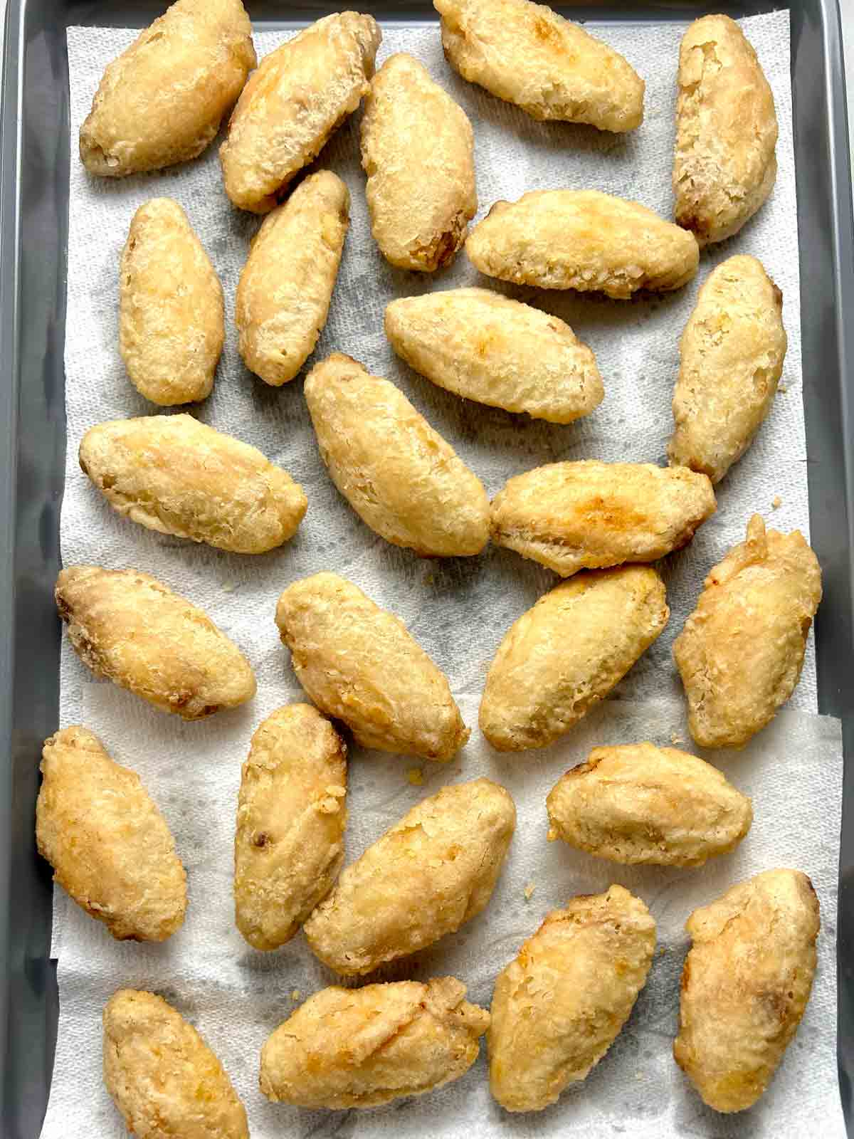 deep-fried chicken wings drying on paper towel-lined baking sheet.