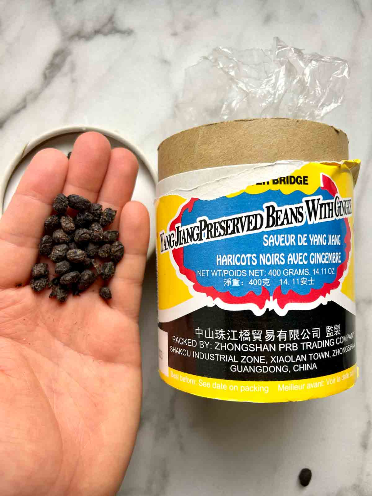 hand holding handful of fermented black beans next to its container.