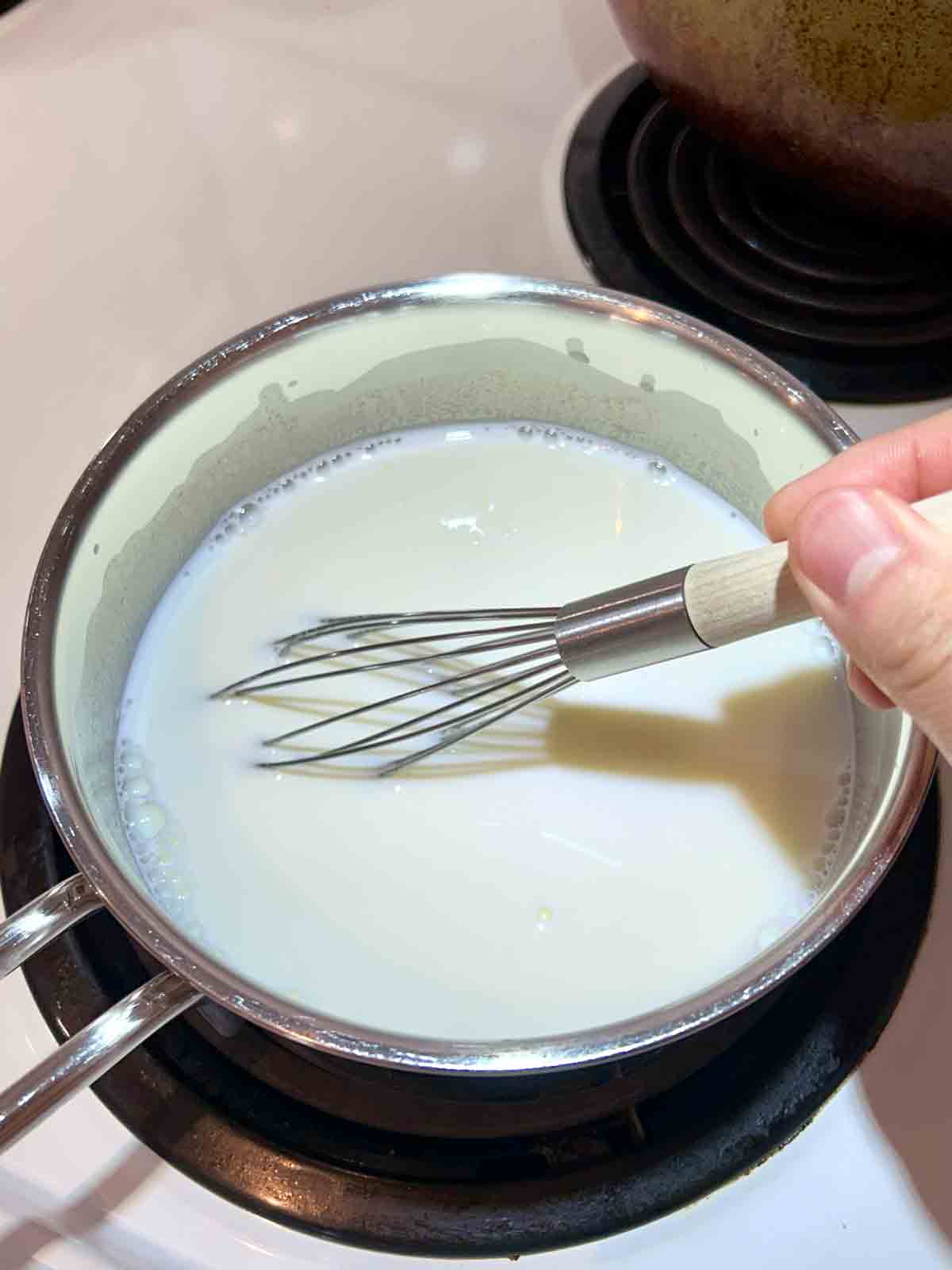 sugar and milk being whisked in saucepan.