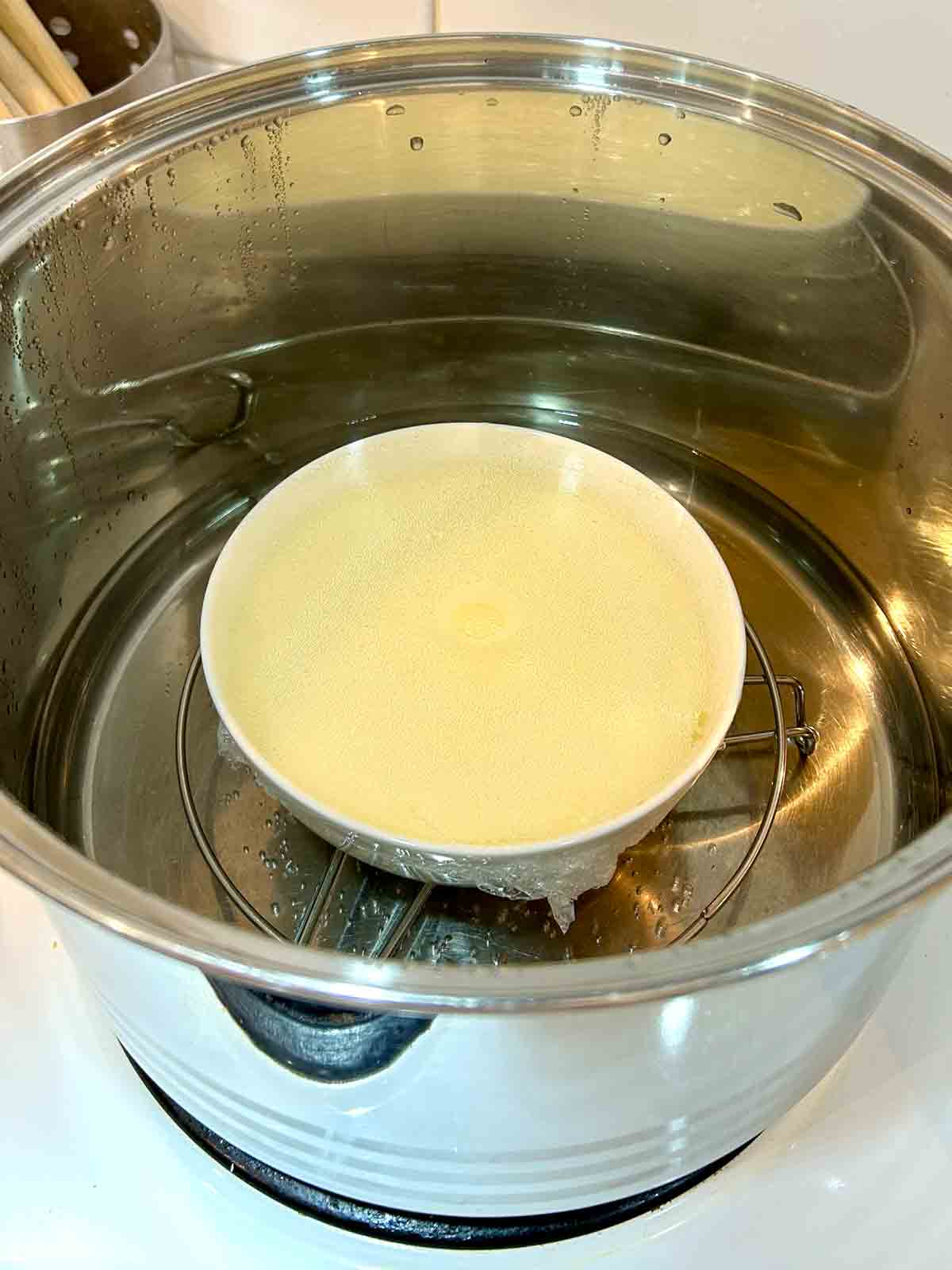 bowl of egg pudding covered with plastic wrap, steaming in a pot.