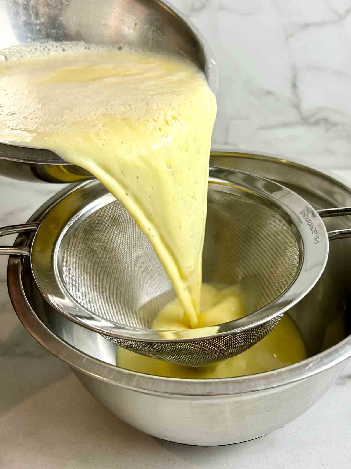 egg and milk mixture being poured through a fine sieve.