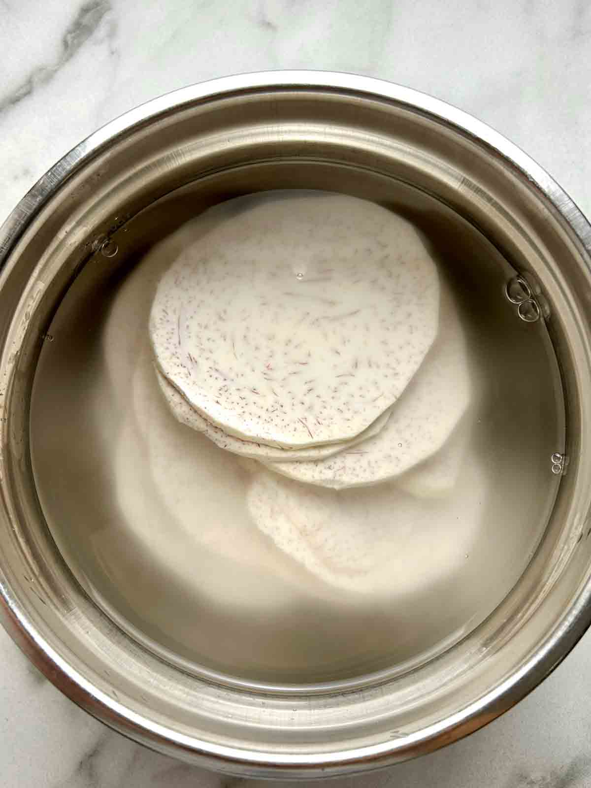 taro slices being soaked in bowl of water.