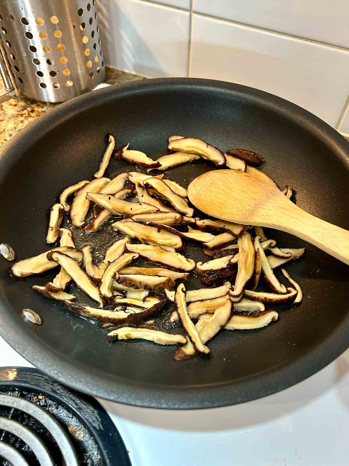 shiitake mushrooms being cooked in pan.