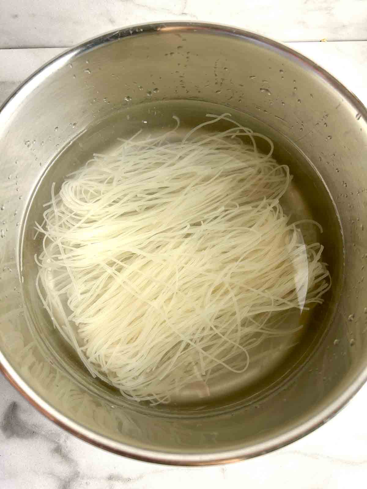 dried rice noodles soaking in pot of water.