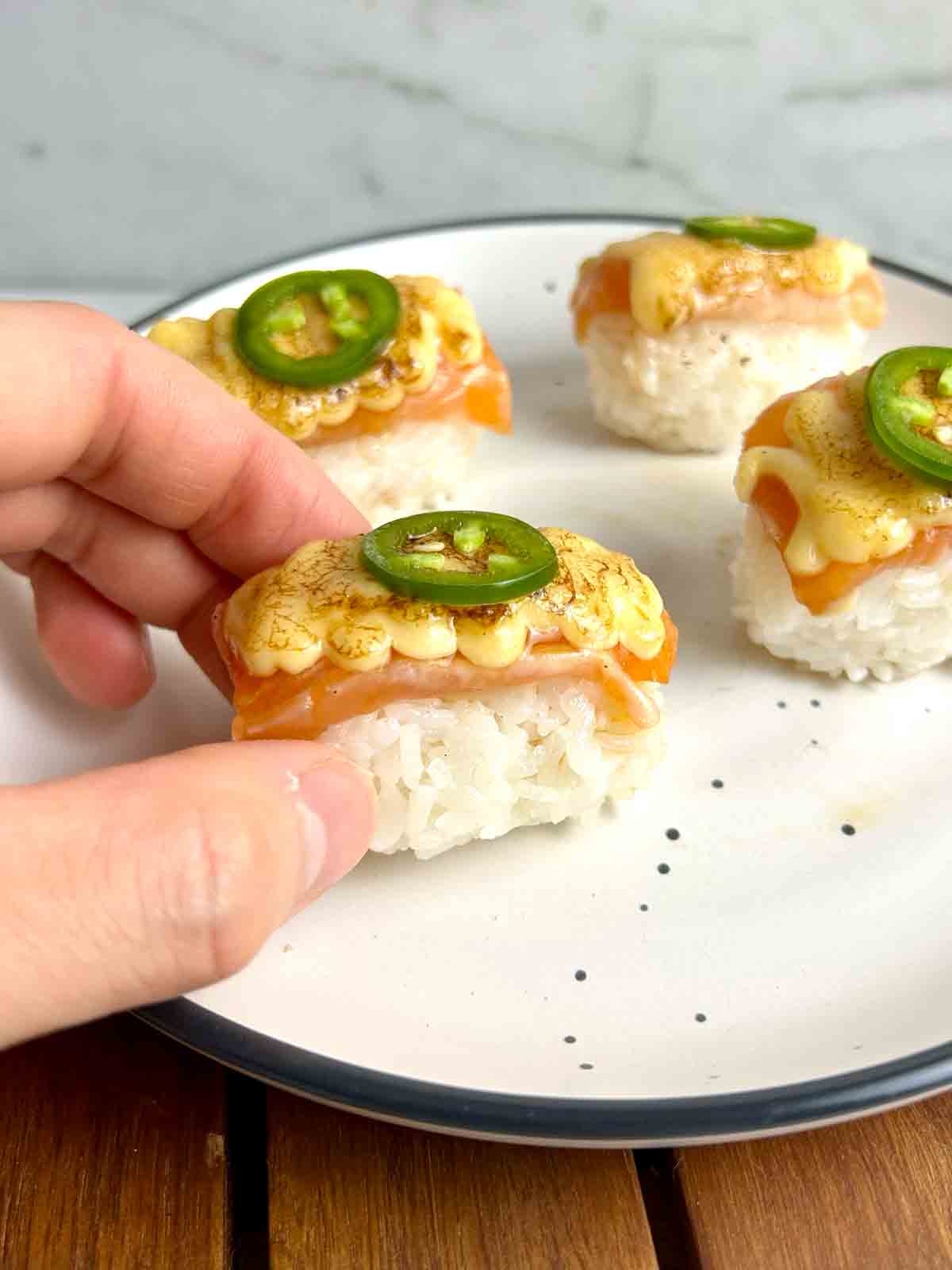 hand lifting piece of aburi salmon from plate.