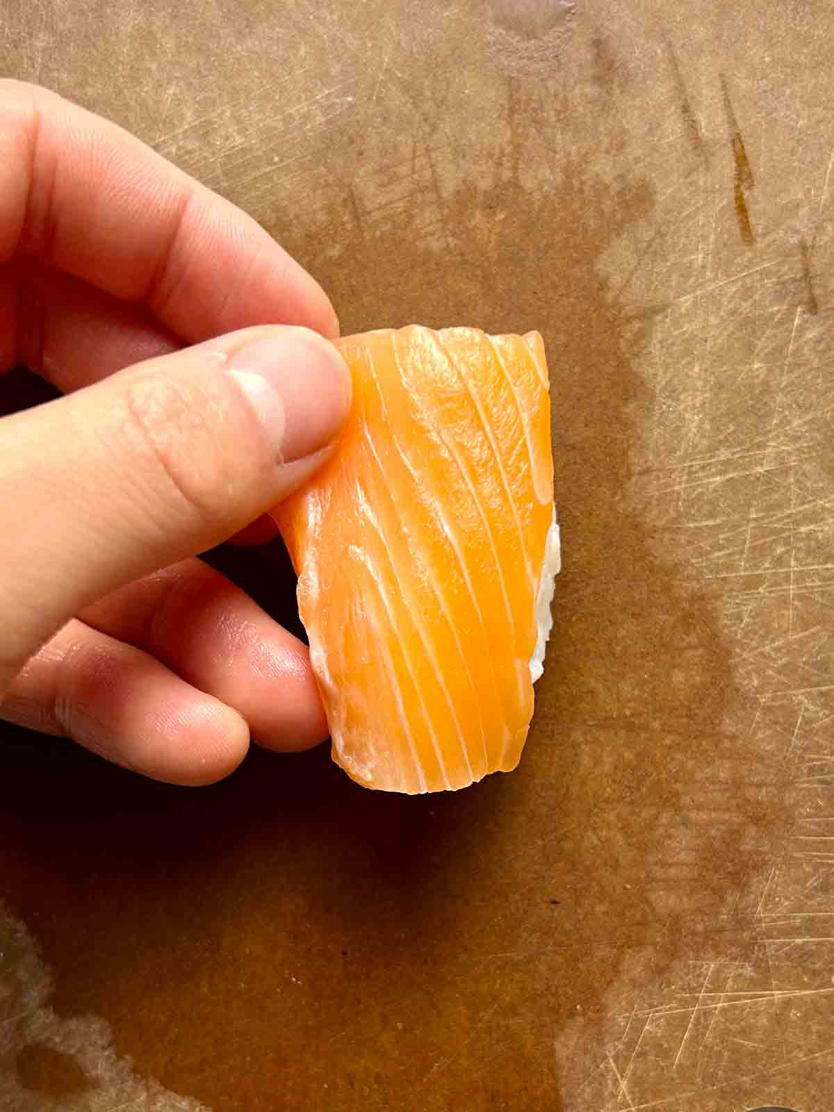 slice of salmon being placed on ball of rice.