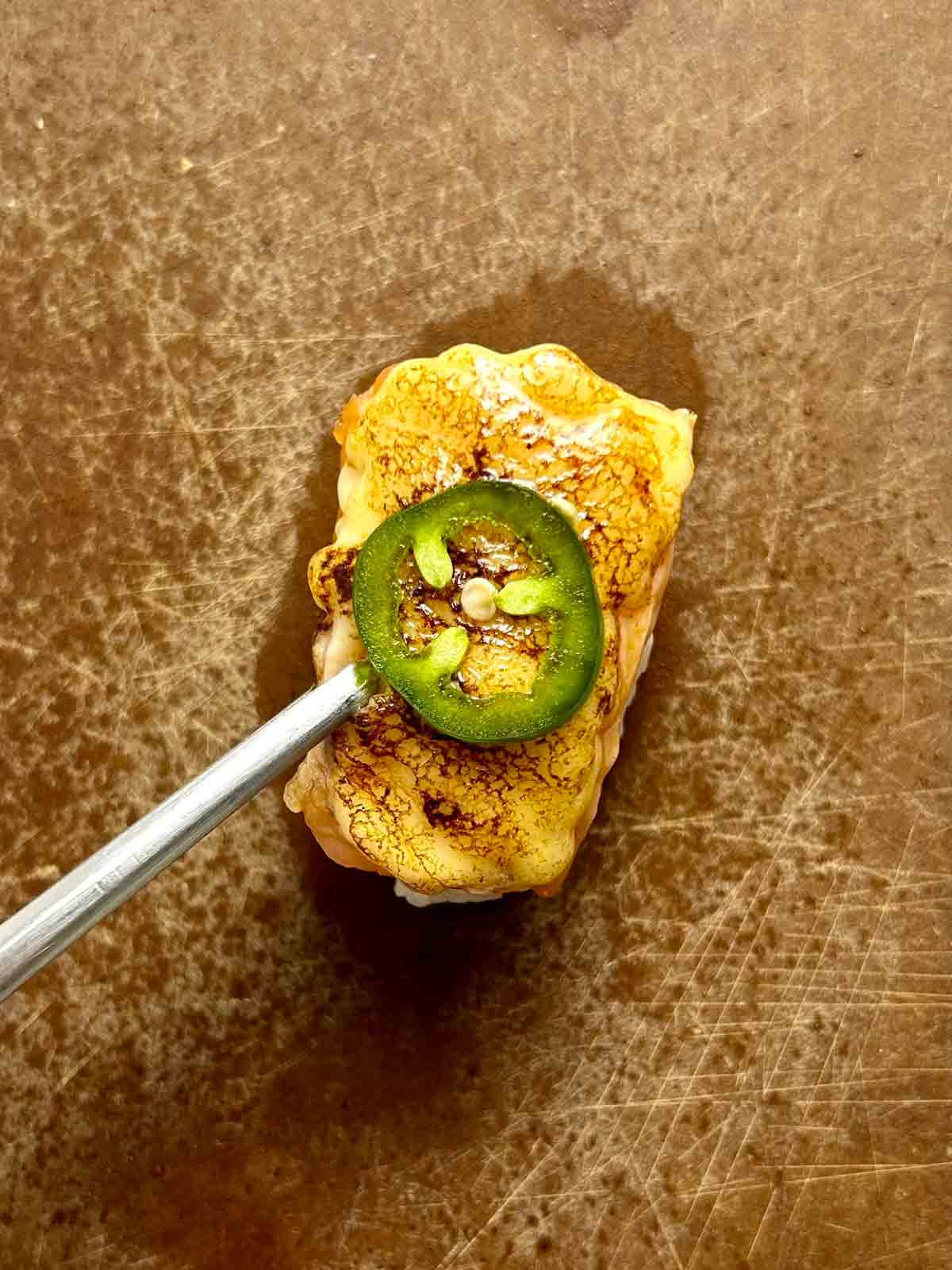 slice of jalapeno being placed on top of aburi.