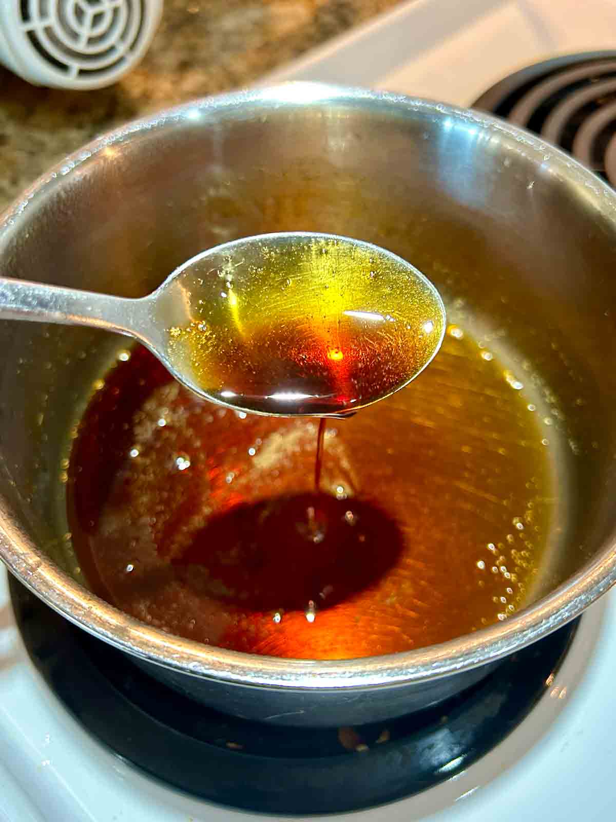 spoon lifting soy glaze from saucepan.