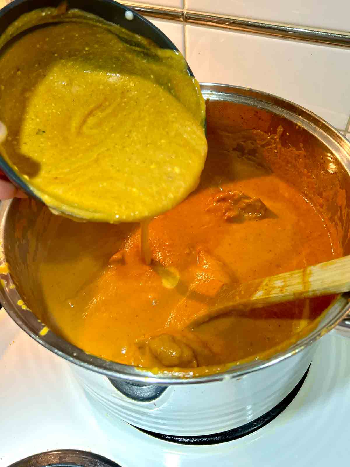 yogurt mixture being added to pot of butter chicken gravy.