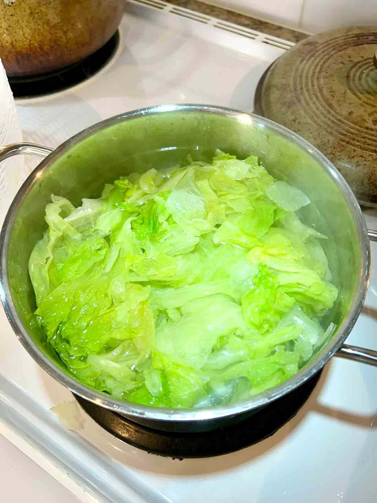 lettuce being boiled in pot of water.