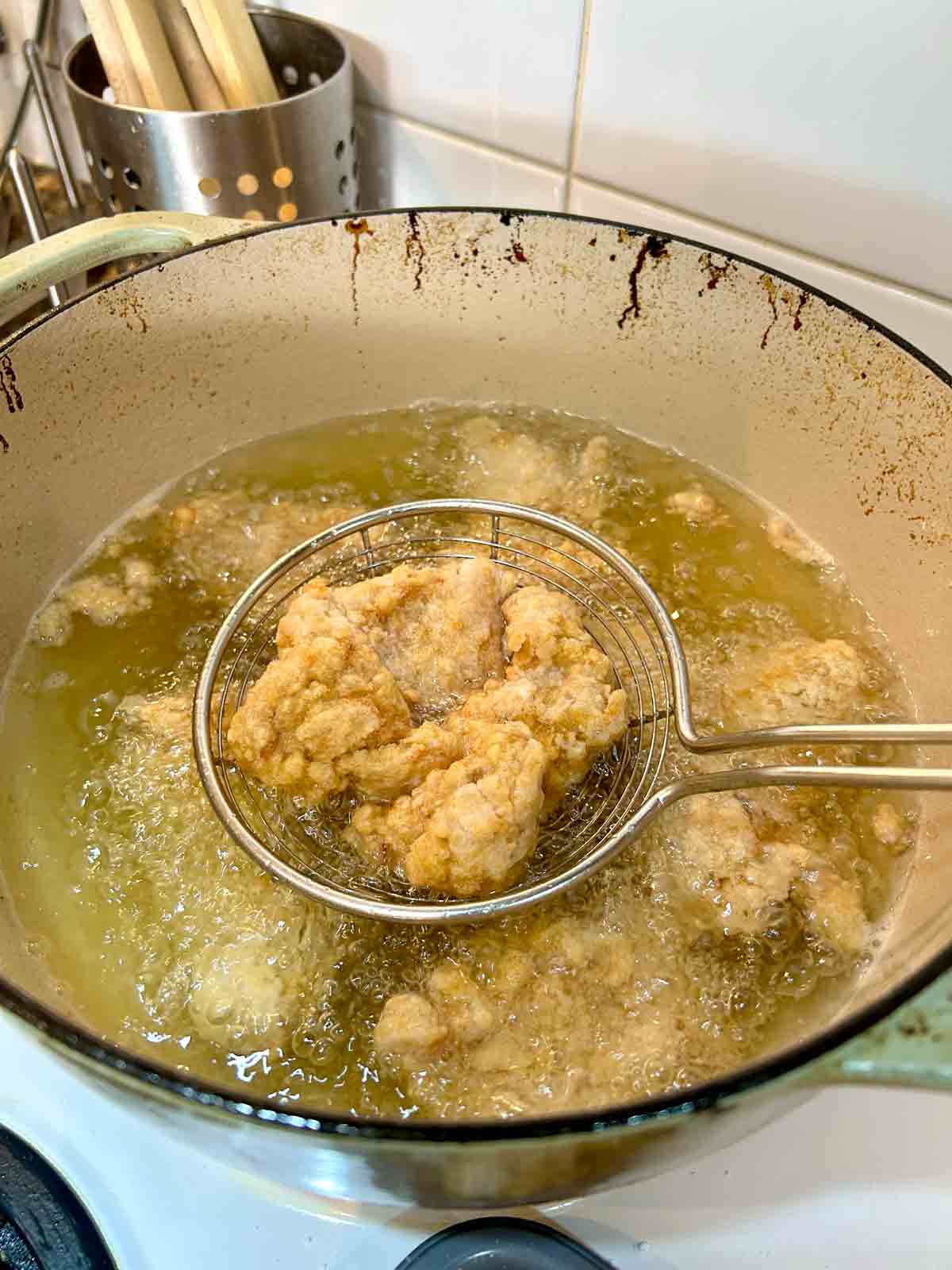 metal spider lifting out fried chicken pieces from oil.