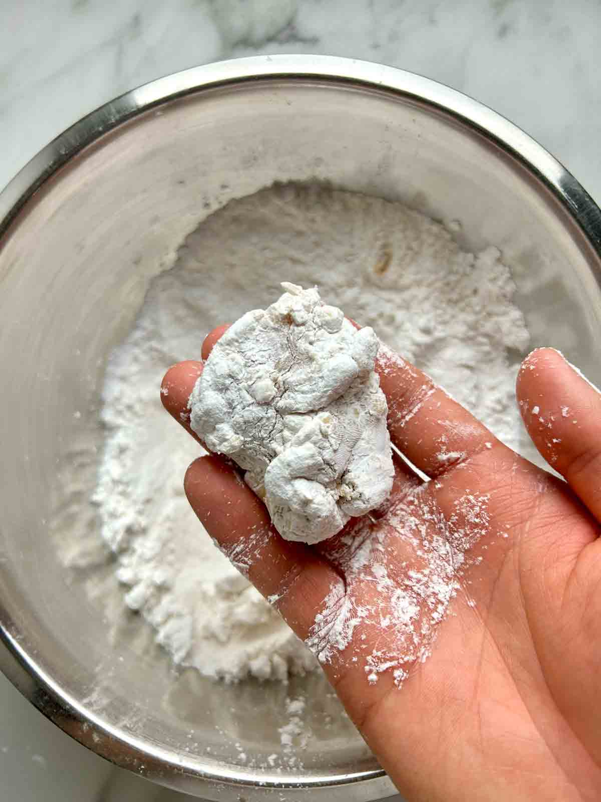 piece of chicken being coated in starches.