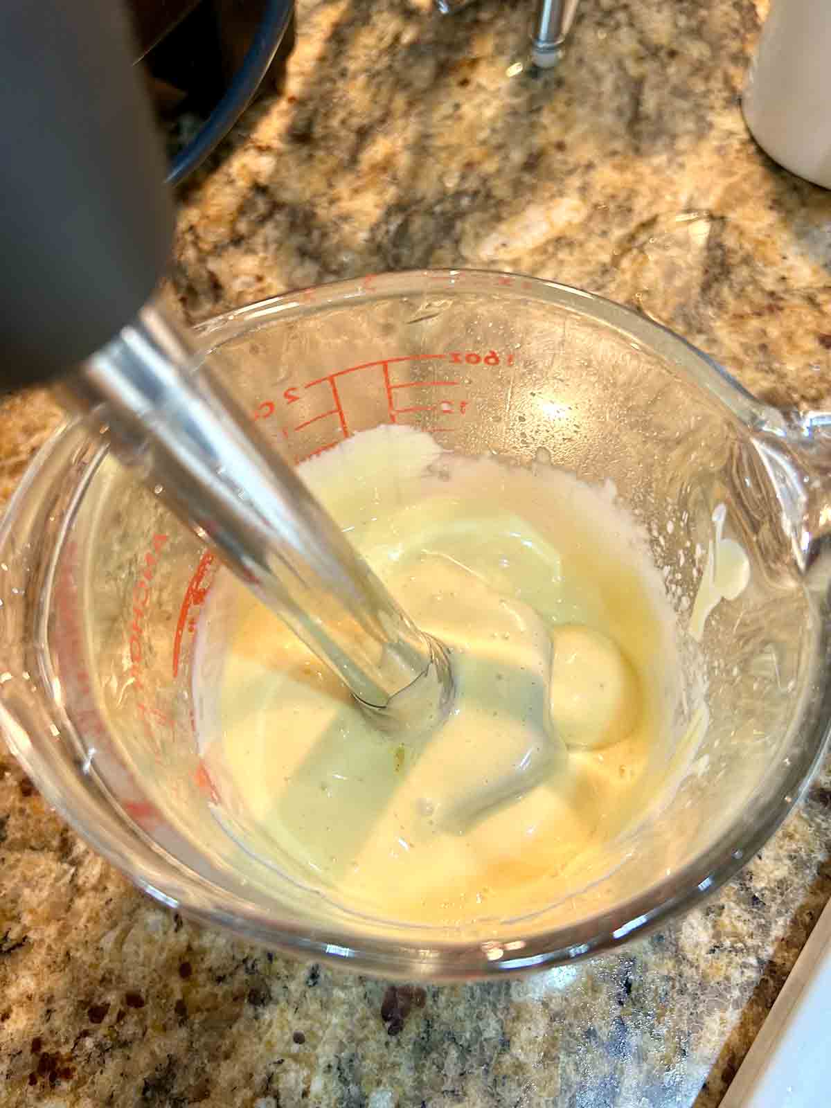 hollandaise being blended in measuring cup with immersion blender.